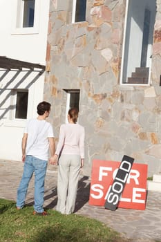 Rear view of couple holding hands and looking at their new house