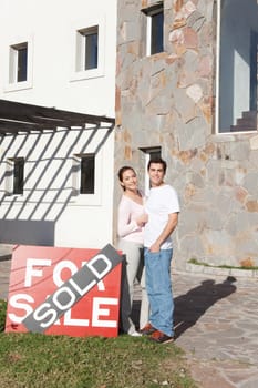 Couple standing near house sold sign outside home