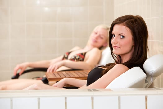 Two women relaxing in chairs beside an indoor pool
