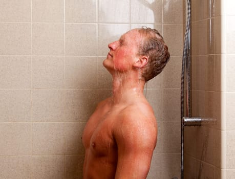 Torso of a man showering with head back, water on face