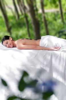 Beautiful young girl at the day spa with black stones on her bare back