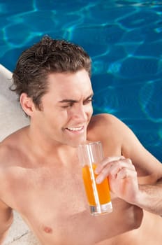 Handsome man by the poolside with a glass of orange juice