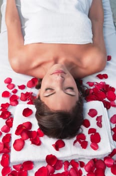 Relaxed woman lying on a massage table in a spa center with rose petals around