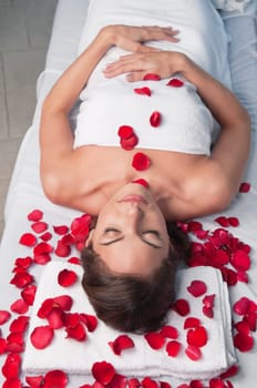 Beautiful relaxed woman lying on a massage table with rose petals around