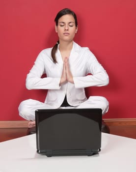 Attractive businesswoman meditating in yoga lotus position with laptop on table