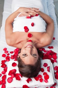 Smiling beautiful woman lying on a massage table with rose petals around
