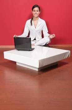 Young beautiful businesswoman sitting in yoga lotus position with laptop on table