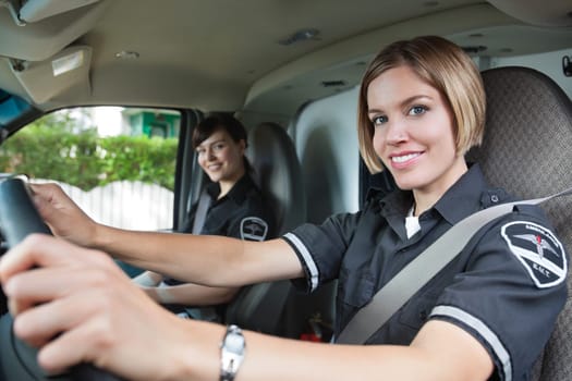 Portrait of happy female paramedic driving ambulance with team member in background