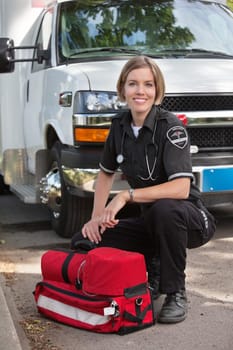 Portrait of a happy paramedic kneeling by a portable oxygen unit and ambulance