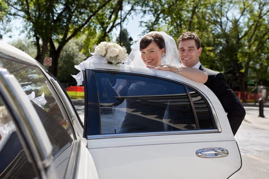 Happy wedding couple getting in car and looking at camera