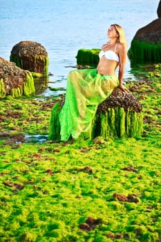 Beautiful woman like mermaid posing on the rock