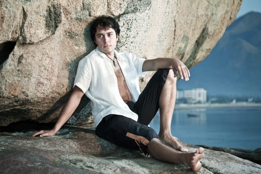 Handsome man is sitting on the rocky cape