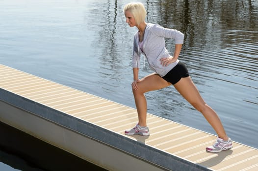 Sport young woman stretch body on water pier sunny day