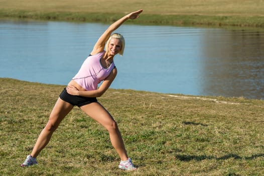 Young woman stretching outdoors before jogging workout river bank summer