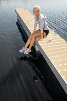 Smiling sport woman relax on pier water sunny day