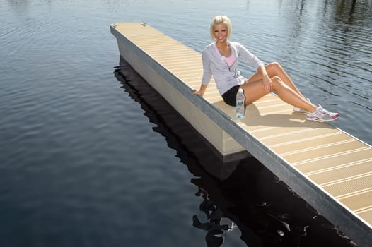 Smiling sport woman relax on pier water sunny day