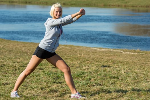 Young woman stretching outdoors before jogging workout river bank summer