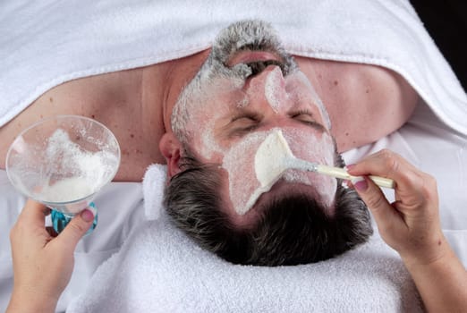 Hand of beautician massaging the forehead of mature man having a facial.