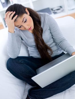 Worried young woman sitting on couch and working on laptop