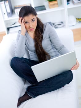 Worried young woman sitting on couch and working on laptop