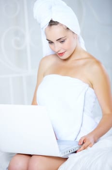 Portrait of cute teenage girl on white bed with laptop