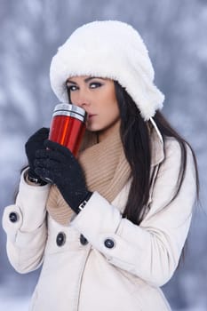 Beautiful woman holding thermal mug in snowy winter outdoors