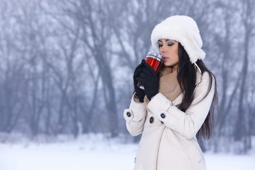 Beautiful woman holding thermal mug in snowy winter outdoors