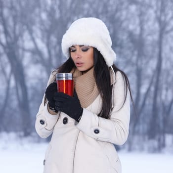 Beautiful woman holding thermal mug in snowy winter outdoors