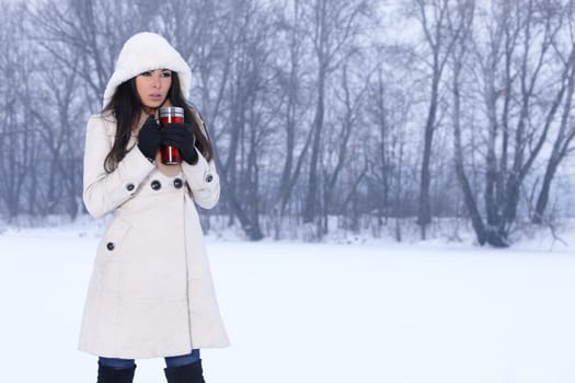 Beautiful woman holding thermal mug in snowy winter outdoors