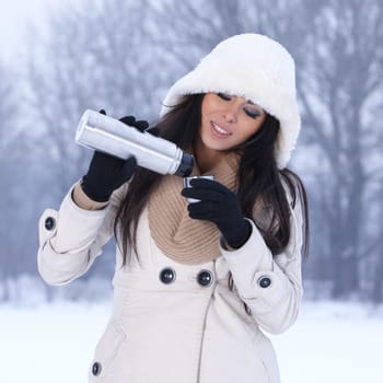 Beautiful woman holding thermos in snowy winter outdoors