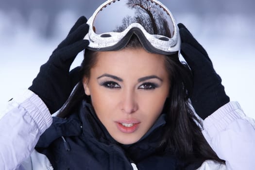 Beautiful woman wearing goggles in snowy winter outdoors