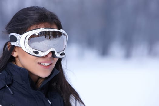 Beautiful woman wearing goggles in snowy winter outdoors