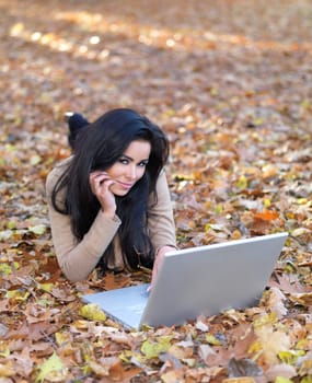 Beautiful woman working on laptop in park during autumn season