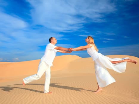 Young couple dancing on desert dune in white clothes