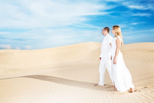 Young couple walking on desert dune in white clothes