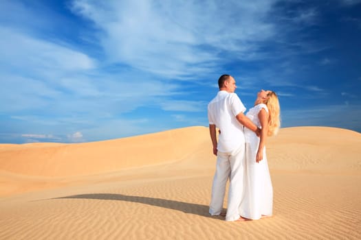 Young couple on desert dunes in white clothes