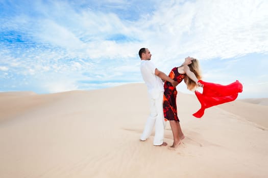 Young couple dancing on desert dune with red scarf