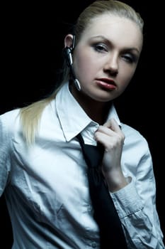 Beautiful business woman wearing black tie and white shirt isolated on black background talking via wireless headset
