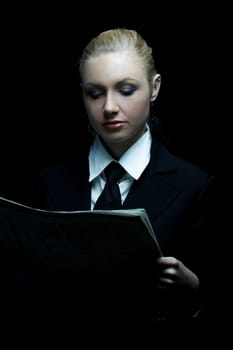 Beautiful business woman wearing black tie and jacket isolated on black background holding newspaper