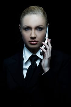 Beautiful business woman wearing black tie and jacket isolated on black background with cell phone