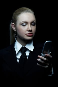 Beautiful business woman wearing black tie and jacket isolated on black background with cell phone