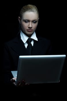 Beautiful business woman wearing black tie and jacket isolated on black background with laptop computer
