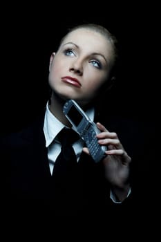 Beautiful business woman wearing black tie and jacket isolated on black background with cell phone