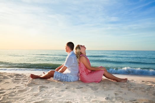 Couple sitting on the beach at sunrise time.