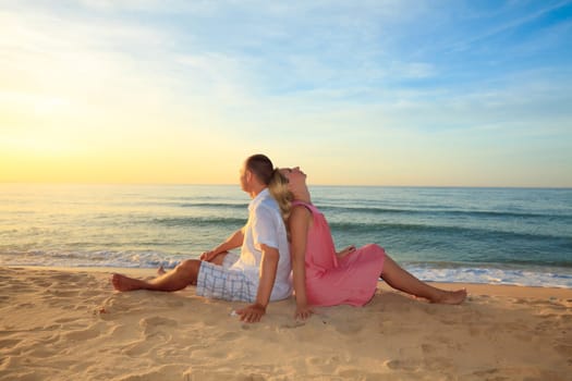 Couple sitting on the beach at sunrise time.