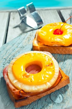 Exotic open ham and pineapple sandwich topped with a ring of golden melted cheese sreved on a deck alongside a pool
