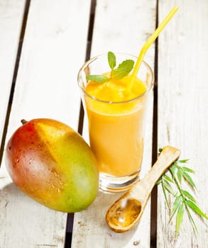 High angle view of a glass of healthy fresh mango smoothie with a delicious ripe whole fruit alongside on wooden decking