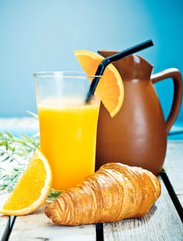 Healthy tropical breakfast consisting of a chilled glass of freshly squeezed orange juice and a crisp croissant on a deck overlooking th sea