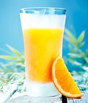 Tall glass of chilled orange cocktail with freshly squeezed juice against a blue summer sky