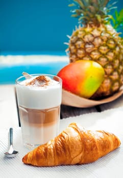 Healthy tropical snack of a crisp buttery croissant served with a creamy layered Latte Macchiato at the sea